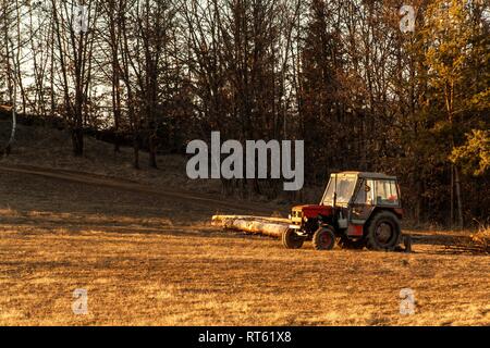 Old red tractor on the edge of a forest. Work in forest. An abandoned tractor. Landscape of the Czech countryside. Stock Photo