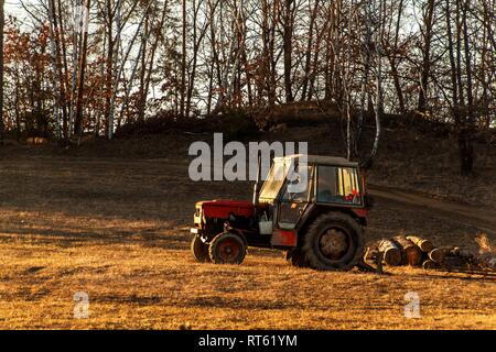 Old red tractor on the edge of a forest. Work in forest. An abandoned tractor. Landscape of the Czech countryside. Stock Photo