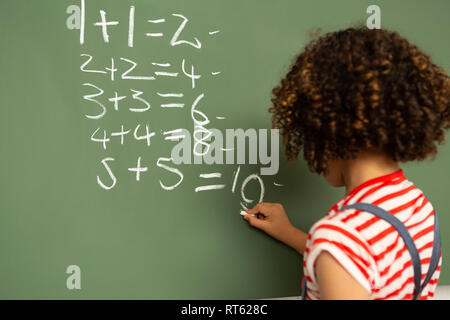 Schoolgirl solving maths formula on green board in classroom Stock Photo