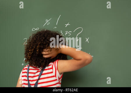 Schoolgirl solving maths formula on green board in classroom Stock Photo