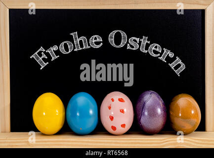 Easter frame with painted eggs and chalkboard. Happy Easter in white chalk. Happy Easter in German : "frohe Ostern" Stock Photo
