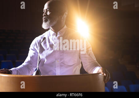 Businessman looking and thinking while standing on stage in auditorium Stock Photo