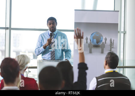 Businesswoman raising hand during business seminar Stock Photo