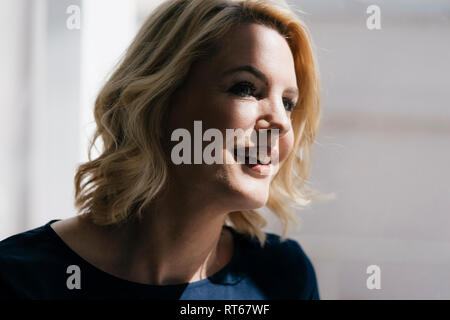 Portrait of smiling blond woman in sunlight at window Stock Photo
