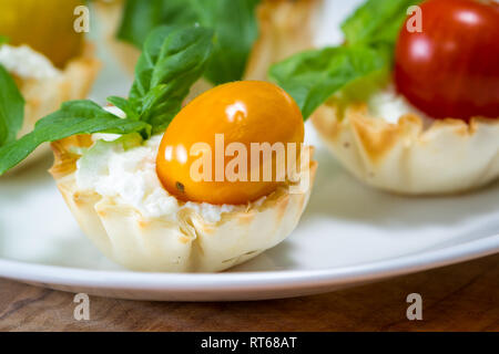 delicious puff pastry cups filled and baked with goat cheese topped with fresh basil and cherry tomato Stock Photo