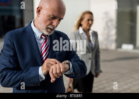 Senior businessman checking the time with businesswoman in background Stock Photo