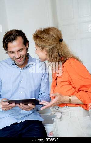 Happy couple working from home, discussing over digital tablet Stock Photo