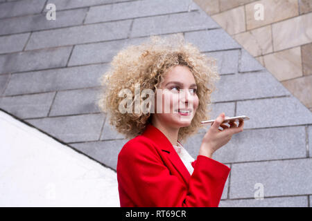 Portrait of smiling blond woman with ringlets wearing red suit coat talking on mobile phone Stock Photo