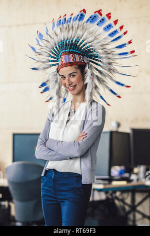 Young woman wearing Indian headdress, standing in office, with arms crossed Stock Photo