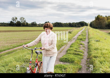 Senior woman pushing bicycle in rural landscape Stock Photo