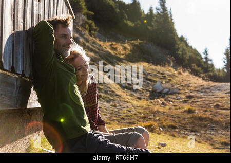 Hiking couple sitting in front of mountain hut, taking a break Stock Photo