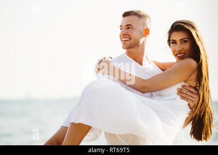 Young happy and joyful Caucasian adult romantic couple in white summer wear - Boyfriend carrying girlfriend on tropical beach and ocean - with copy sp Stock Photo