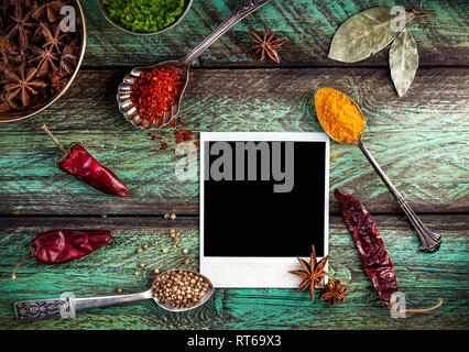 Spices, blank photo frame and dry red chili peppers at wooden green background with spoons nearby Stock Photo