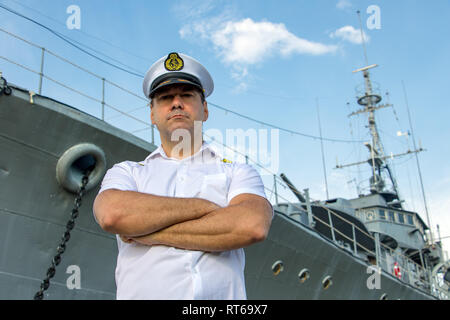 Captain standing in dock before warship and  looking ahead. A sailor officer in white uniform stands beside battleship. Stock Photo