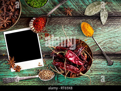 Spices, blank photo frame and dry red chili peppers at wooden green background with spoons nearby Stock Photo