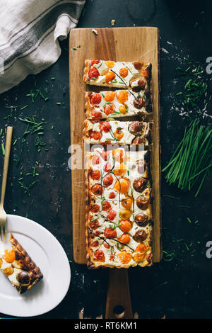 Homemade pie ( quiche) with ricotta, fresh colored tomatoes ,rectangular shapes on a cutboard, top view, dark board. Stock Photo
