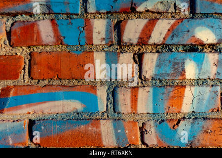 Old red brick wall with blue and white graffiti fragments, viewed in close-up Stock Photo