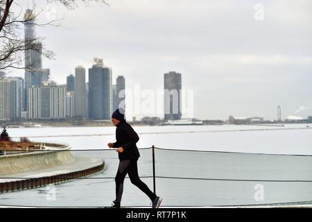 Chicago, Illinois, USA. A lone runner jogs along the Chicago Museum Campus in front of an ice-laden Lake Michigan and a portion of the city skyline. Stock Photo