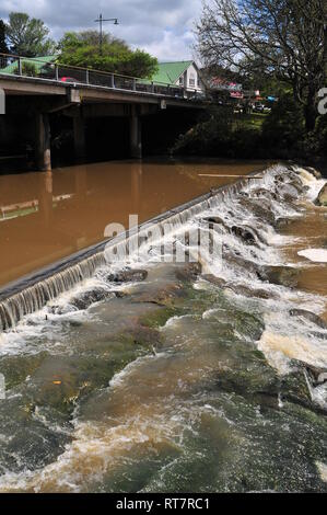Vertical view of small dam with stone cascades right next to bridge on very dirty and muddy river. Stock Photo