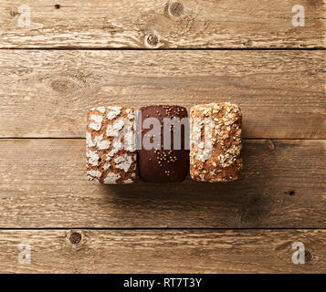 Three loaves of bread on wooden table. Bakery concept with empty space for design. Gluten-free rye bread with bran and coriander Stock Photo