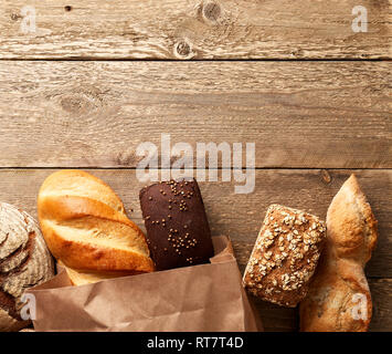 Assortment of fresh baked bread on a wooden background. White and rye bread in a paper bag. Bakery concept with copy place