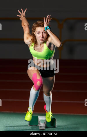 Female athlete starting sprint race running from blocks against dark background Stock Photo