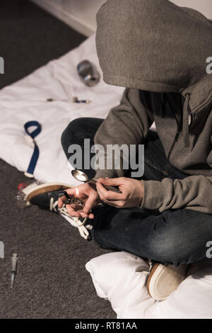 junkie man in hood heating spoon with heroin on lighter Stock Photo