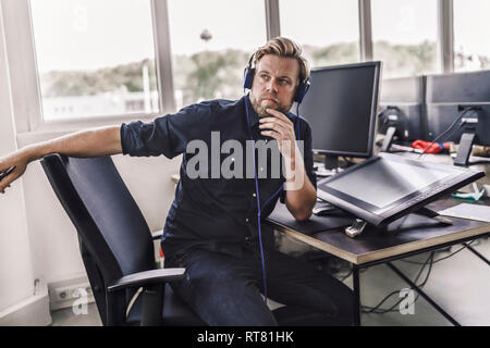Tired graphic designer using digital tablet, wearing headphones Stock Photo