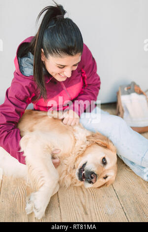 Happy young woman stroking and playing with her golden retriever dog Stock Photo