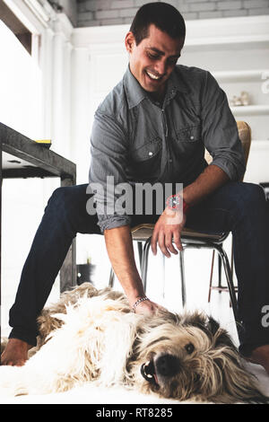 Young man sitting at desk stroking dog Stock Photo