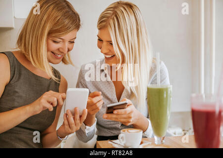 Two happy young women with smartphones in a cafe Stock Photo