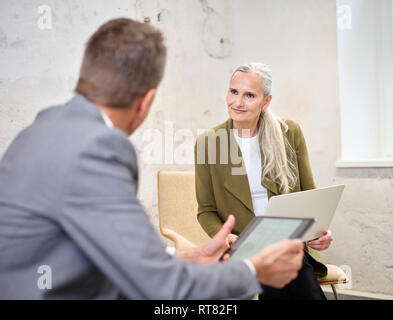 Businessman and businesswoman with laptop and tablet in modern office Stock Photo