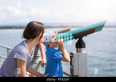 Germany, Friedrichshafen, Lake Constance, mother with son looking through telescope at lakeshore Stock Photo