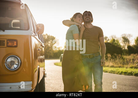 Affectionate couple walking on the road with arms around, next to their camper Stock Photo