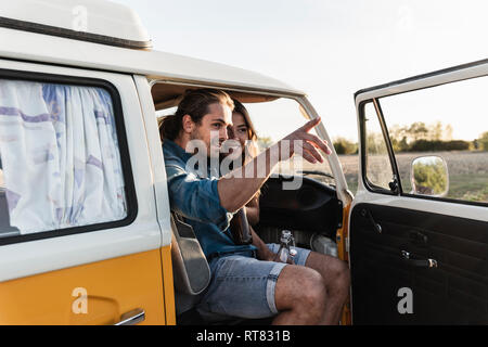 Happy couple sitting in their camper, man pointing at distance Stock Photo