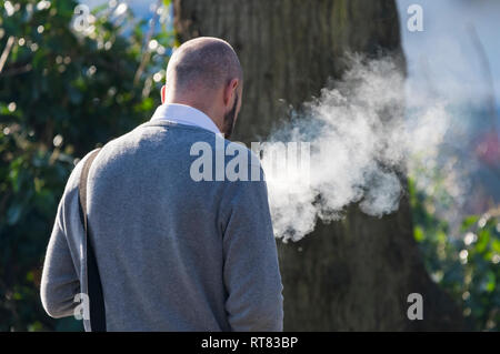 Caucasian man walking while vaping, emitting large amounts of smoke, in the UK. Electronic cigarette. Stock Photo