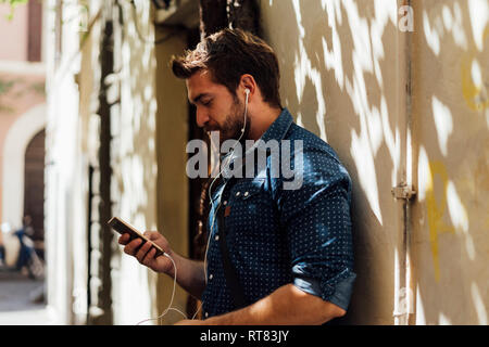 Man using earphones and smartphone outdoors Stock Photo