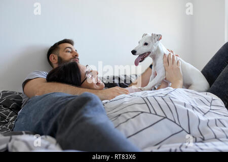 Couple lying on bed cuddling dog Stock Photo