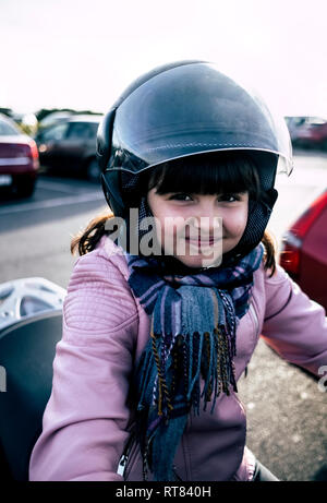 Portrait of smiling little girl on a motorcycle wearing helmet and pink leather jacket Stock Photo