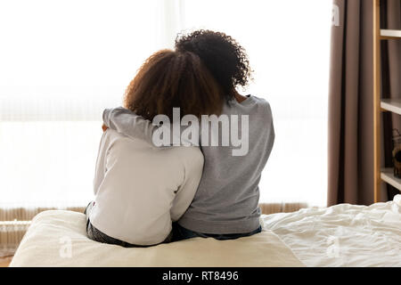Rear view african mother and daughter embracing sitting on bed Stock Photo