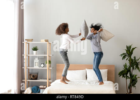 African mother and daughter enjoying pillow fight jumping on bed Stock Photo