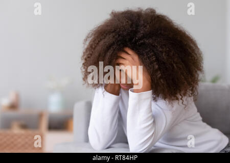 Unhappy african teenager girl thinking about problems sitting on couch Stock Photo
