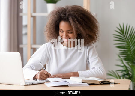 Positive african schoolgirl sitting at desk and study Stock Photo