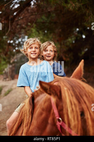 Portrait of two happy boys on horse in a forest Stock Photo