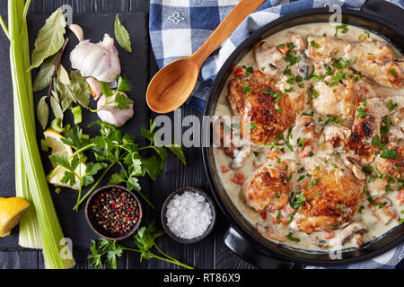 chicken fricassee in a black dutch oven - chicken meat browned and braised in white wine creamy sauce with mushrooms and vegetables, classic french re Stock Photo