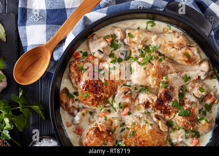 chicken fricassee in a black dutch oven - chicken meat browned and braised in white wine creamy sauce with mushrooms and vegetables, classic french re Stock Photo