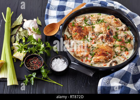 chicken fricassee in a black dutch oven - chicken meat browned and braised in white wine creamy sauce with mushrooms and vegetables, classic french re Stock Photo