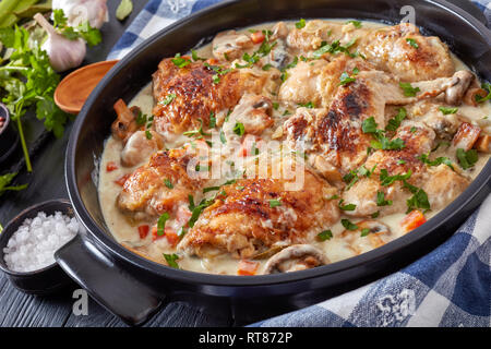 close-up of hot chicken fricassee in a black dutch oven - chicken meat browned and stewed in white wine cream sauce with mushrooms and vegetables, cla Stock Photo