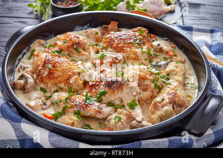 hot chicken fricassee in a black dutch oven on a black table - chicken meat browned and stewed in white wine cream sauce with mushrooms and vegetables Stock Photo