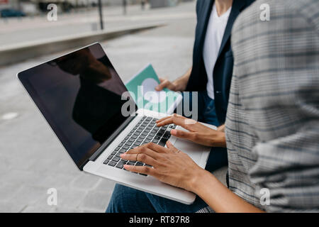 Close-up of two colleagues working together on laptop outdoors Stock Photo